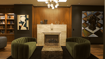 A living room with a fireplace, two green chairs, and a bookshelf.